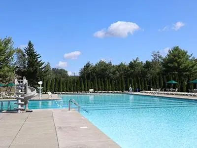 a large blue swimming pool with trees in the background at Cabin Retreat with Hot Tub in Pocono Country Place