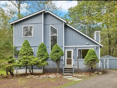 a gray house with trees in front of it at Cabin Retreat with Hot Tub in Pocono Country Place