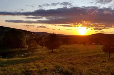 a sunset in a field with the sun setting at Gorgeous Finger Lakes Accommodation near Ithaca for Glamping in New York in Brooktondale