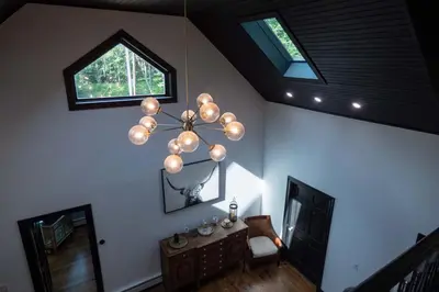 a chandelier in a living room with a table and a window at Chic Catskills Farmhouse in Harris