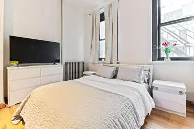 a white bedroom with a bed and a flat screen tv at XL Prime Tribeca Furnished Loft, June To Aug 90 Days Stay Required in New York