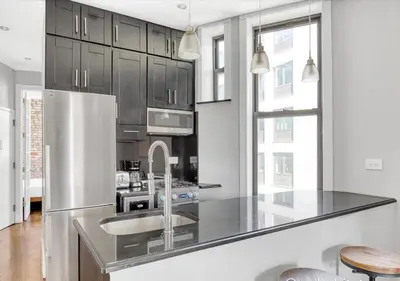 a kitchen with black cabinets and a stainless steel refrigerator at Midtown West Furnished Apartment 3BR in New York