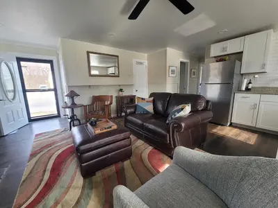 a living room with leather furniture and a kitchen at Riverfront Cottage in Owego in Owego