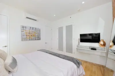 a white bedroom with a bed and a flat screen tv at Spacious 2BR 2BA with Rooftop Walk to Times Square, June To Aug 90 Days Stay Required in New York