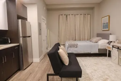 a living room with a bed and a chair and a kitchen at Private Studio 5 minutes to the NYC train in Bayonne