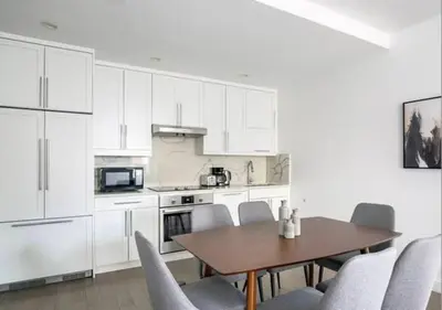 a kitchen with white cabinets and a wooden table and chairs at 3BR Furnished Loft in Midtown West in New York