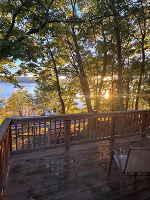 a deck with the sun shining through the trees at Cayuga lake cottage with private lake access in Washingtonville