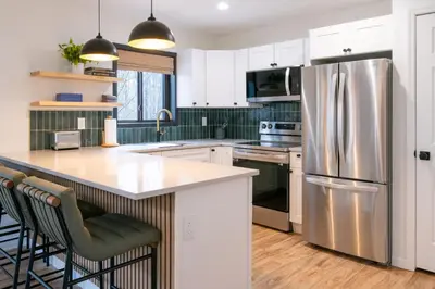 a kitchen with a stainless steel refrigerator and white cabinets at Scandinavian Retreat Hot Tub, Pool, Game Rm in Gouldsboro