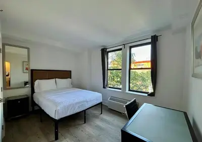 a bedroom with a bed and a table and two windows at Central Park West Furnished 1 Bedroom Apartment in New York
