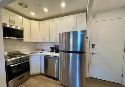 a stainless steel refrigerator in a kitchen with white cabinets at Central Park West Furnished 1 Bedroom Apartment in New York