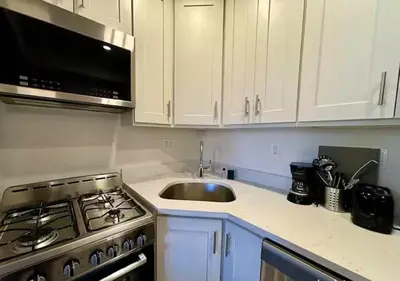 a kitchen with white cabinets and a stove and a sink at Central Park West Furnished 1 Bedroom Apartment in New York