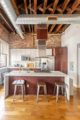 an industrial kitchen with a large counter and stools at Stylish SOHO-Inspired Loft, 15 Min to NYC Times Square in Union City
