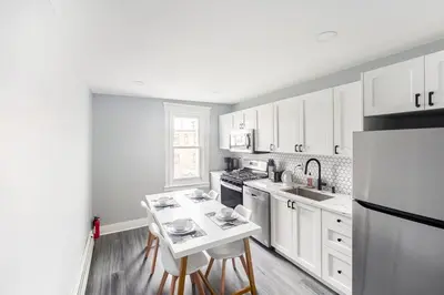 a kitchen with white cabinets and a table and a refrigerator at Prime Location Explore NYC in West New York