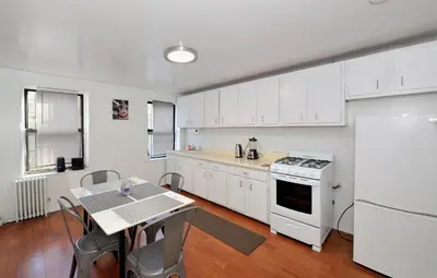 a kitchen with white cabinets and a table and a stove at Cozy 2BR Apartment in the Heart of Chelsea in New York