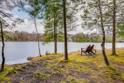 a person sitting on a bench next to a lake at Lakefront Poconos Cabin with Deck and Game Room in Pocono Lake
