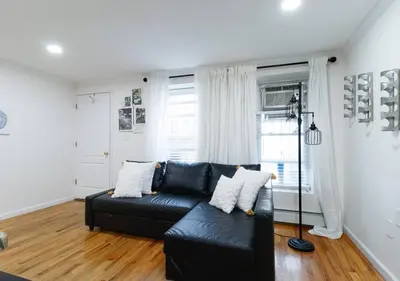 a living room with a black leather couch and wooden floors at Midtown West Furnished 3 Bedroom Apartment in New York