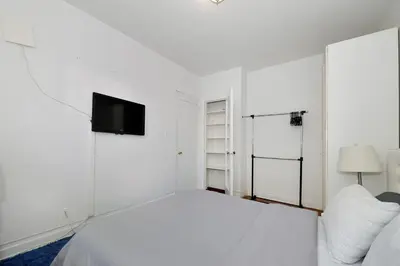 a white bedroom with a bed and a flat screen tv at Midtown West Furnished 3 Bedroom Apartment in New York