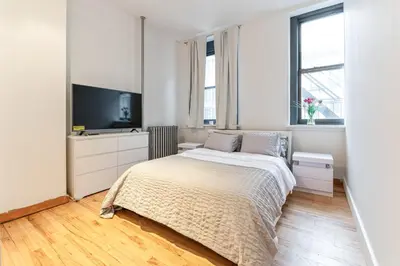 a white bedroom with a bed and a flat screen tv at XL Prime Tribeca Furnished Loft in New York