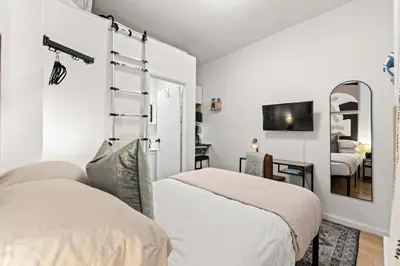 a white bedroom with two beds and a mirror at Micro Studio Walk to Time Square in New York