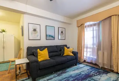 a living room with a black couch and yellow pillows at Sunny Fully Furnished Studio in Chelsea in New York