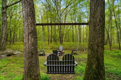 a bench sitting between two trees in a park at Perfect Couples Cabin Fireplace Firepit & Wine Nearby in Hawley