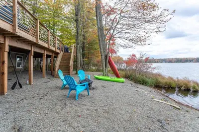 three chairs and a canoe on the shore of a lake at Tranquil Shores Waterfront Fire Pit Hammock in Tobyhanna