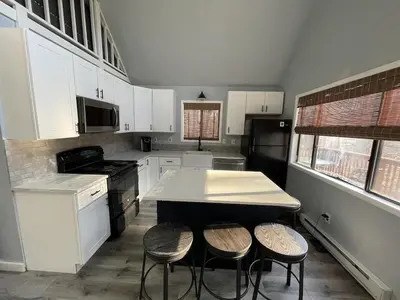 a kitchen with white cabinets and a island with stools at Fully updated home with hot tub in amenity filled community in Lackawaxen