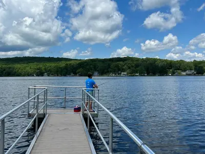 a man fishing on a dock on a lake at Fully updated home with hot tub in amenity filled community in Lackawaxen