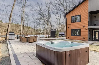 a hot tub on a patio next to a house at Luxury 6BR Mansion - Lakefront, Sauna, Hot Tub in Scotrun