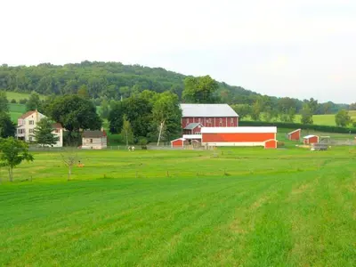 a large green field with a red barn and a farm at Secluded and Rustic Cabin with a Private Deck near Reading, Pennsylvania in Robesonia