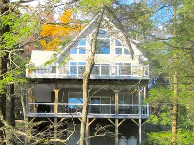 a large house with a deck in the woods at Stunning Weekend Getaway near Hickory Run State Park in Pennsylvania in Jim Thorpe