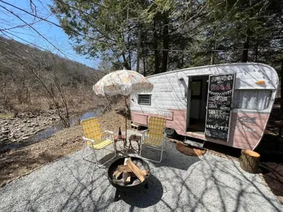 a trailer with chairs and a table and an umbrella at Vintage Shasta Camper for the best of NYC Glamping in Livingston Manor
