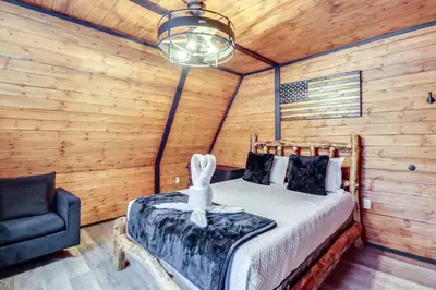 a bedroom with a bed with a lamp and a chair at 9 Mi to Big Boulder Mtn A-Frame Cabin with Hot Tub in Albrightsville