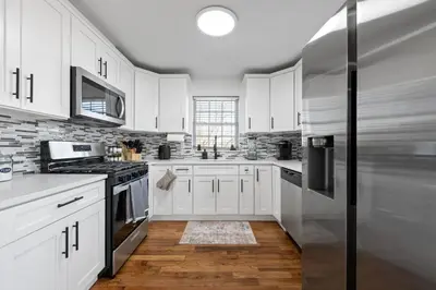 a kitchen with white cabinets and a stainless steel refrigerator at NYC 20min, Sleeps 10, Free Parking, Patio in Bayonne