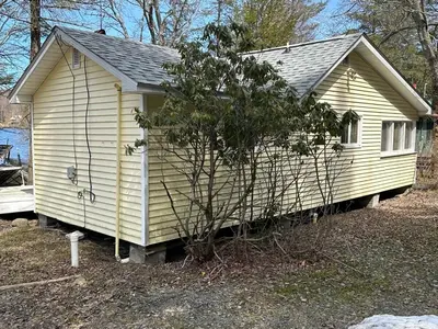 a small yellow house with a tree in front of it at Rustic Lakefront Cabin in Starrucca