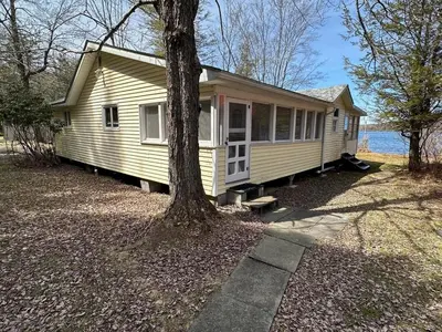 a yellow house with a tree in front of it at Rustic Lakefront Cabin in Starrucca