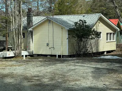 a small yellow house with a tree in front of it at Rustic Lakefront Cabin in Starrucca