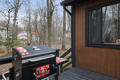 a grill on a deck next to a cabin at 3BR Home w Outdoor Fun Lake Fire Pit Games Grill in Tobyhanna