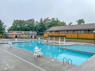 a large swimming pool with chairs in front of a building at 3BR Home w Outdoor Fun Lake Fire Pit Games Grill in Tobyhanna