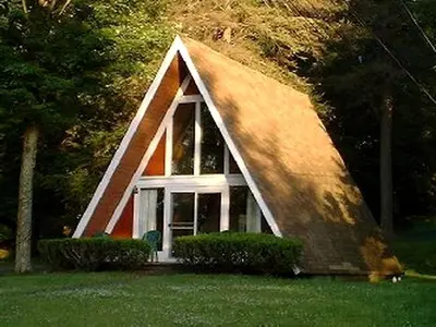 a small house with a triangular roof in the grass at Tranquil Lakeside A-Frame Cabin Rental in Harveys Lake, Pennsylvania in Harveys Lake