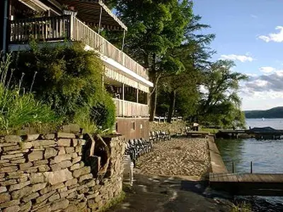 a building with a stone wall next to a body of water at Beautiful Log Cabin Rental in Harveys Lake near Back Mountain, Pennsylvania in Harveys Lake