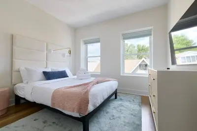a white bedroom with a bed and two windows at Bright 3BR Loft • Hoboken Gem in Hoboken