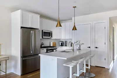 a kitchen with white cabinets and a stainless steel refrigerator at Bright 3BR Loft • Hoboken Gem in Hoboken