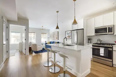 a kitchen with white cabinets and a kitchen island with bar stools at Sunny 2BR Loft • Work Relax Minutes to NYC in Hoboken