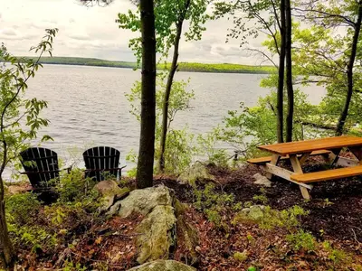a picnic table and two chairs next to a lake at Lakefront Cabin Rental with Incredible Sunsets on Lake Wallenpaupack, Pennsylvania in Hawley