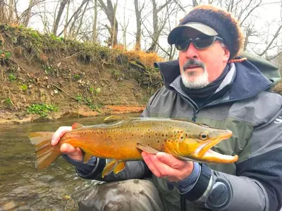 a man holding a brown trout in a river at Stunning Cabin Rental with a Hot Tub Overlooking Fishing Creek near Sproul State Forest, Pennsylvania in Mill Hall
