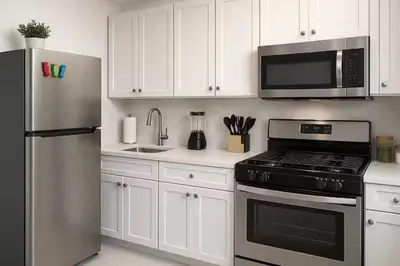 a kitchen with white cabinets and a stainless steel refrigerator at Warm & Cozy Escape - NYC & NWK with Free Parking in Bayonne