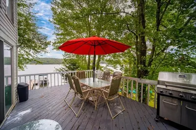 a table and chairs with an umbrella on a deck at Catskills Lakefront with Hot Tub, Sauna and Theater in Monticello