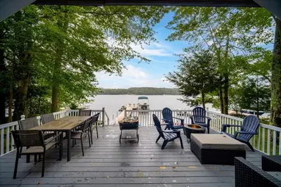 a wooden deck with tables and chairs and a lake at Catskills Lakefront with Hot Tub, Sauna and Theater in Monticello