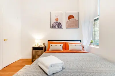 a white bedroom with an orange bed and a window at Aura Style 3BD Suite at Times Square Manhattan in New York